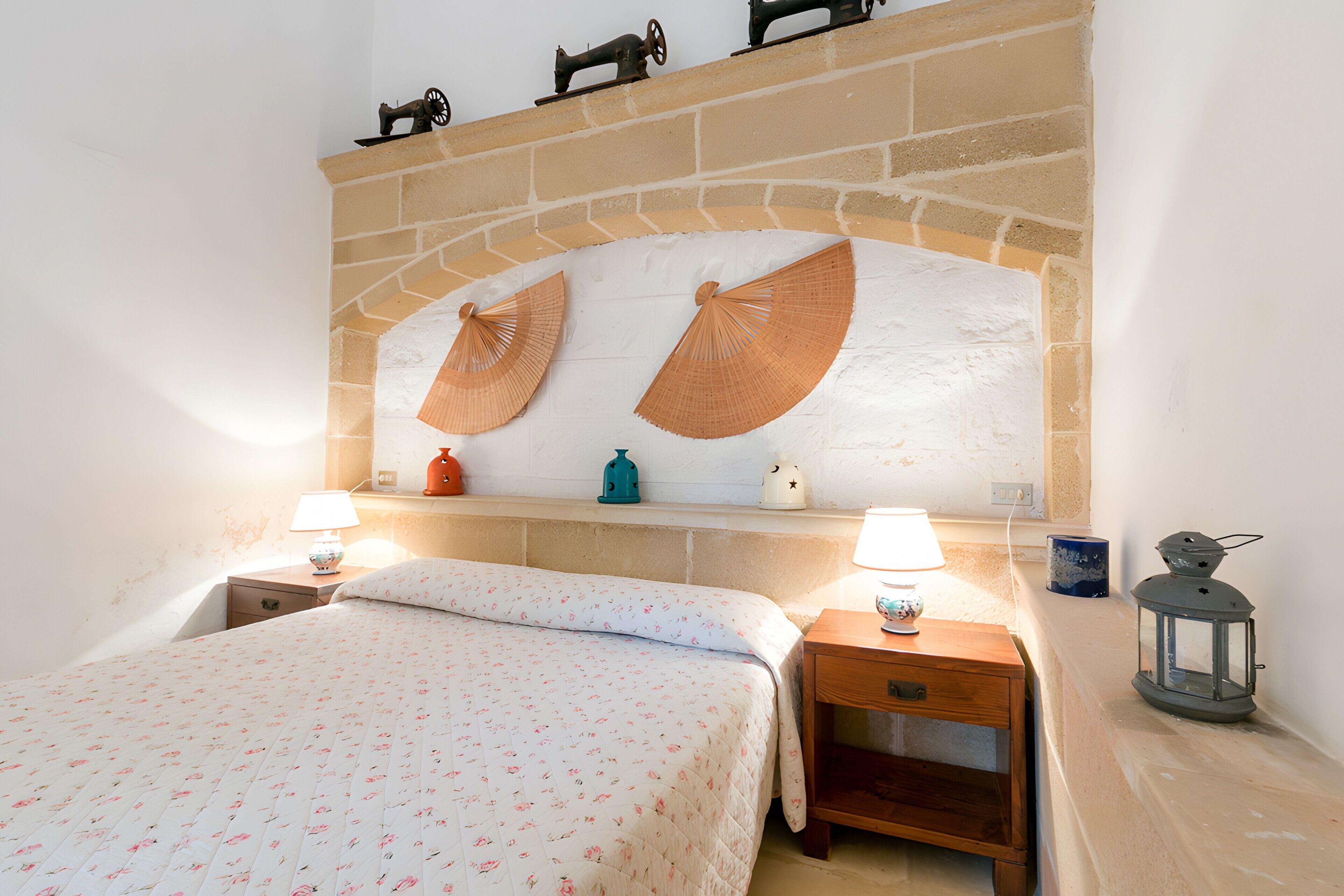A bedroom with a bed, two bedside tables, a nightstand, a brick fireplace, and a shelf with decorative items.