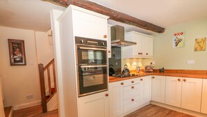 A kitchen with white cabinets, a wooden countertop, and a built-in oven. There are two wall-mounted electrical outlets and a framed picture on the wall. - Little Bargate (Hope Valley)