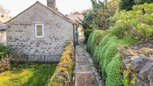 A stone cottage with a small window, a stone pathway, and lush greenery. - Little Bargate (Hope Valley)