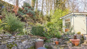 A patio with stone walls, a small table, wicker chairs, and potted plants. - Little Bargate (Hope Valley)