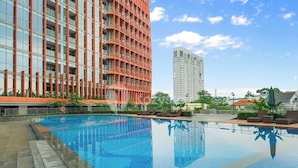 Une piscine dotée d’une terrasse carrelée, entourée de bâtiments modernes avec des balcons, sous un ciel dégagé.