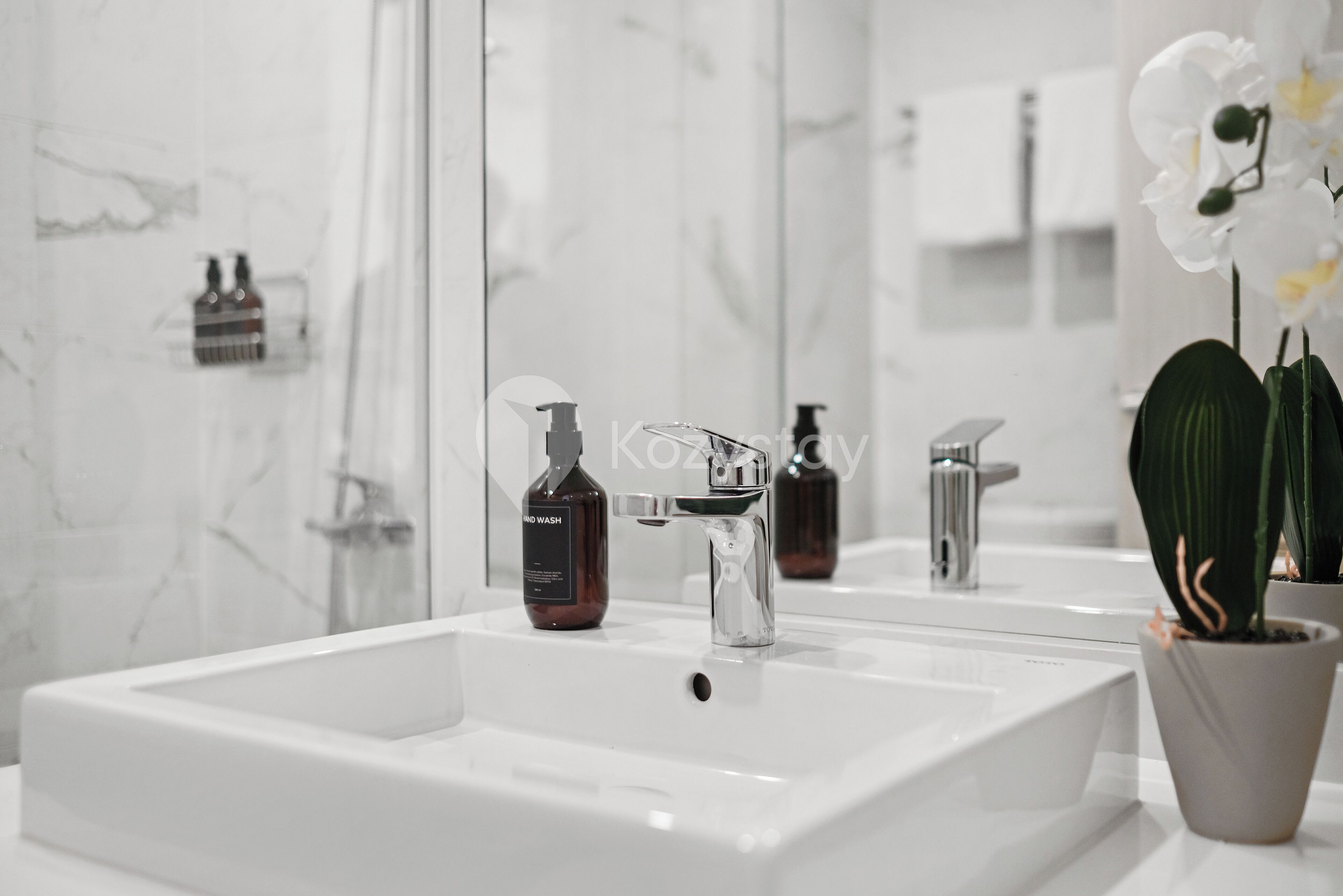 A modern bathroom with a white sink, chrome faucet, and a mirror reflecting the room.