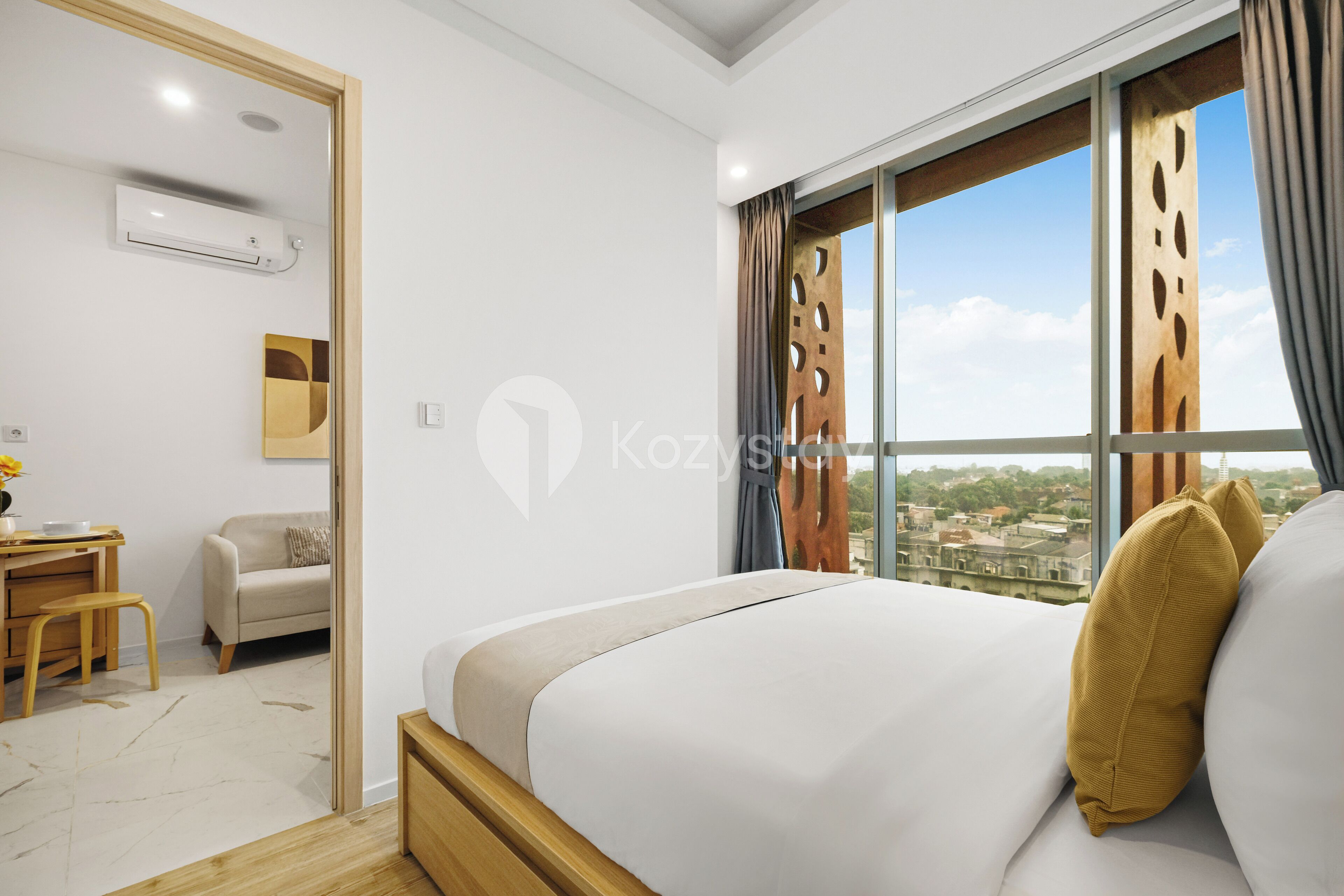 A modern hotel room with a bed, a desk, a chair, and a view of the city through large windows.