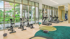 Une salle de sport moderne équipée de machines de cardio, d’un miroir et offrant une vue sur la verdure environnante.