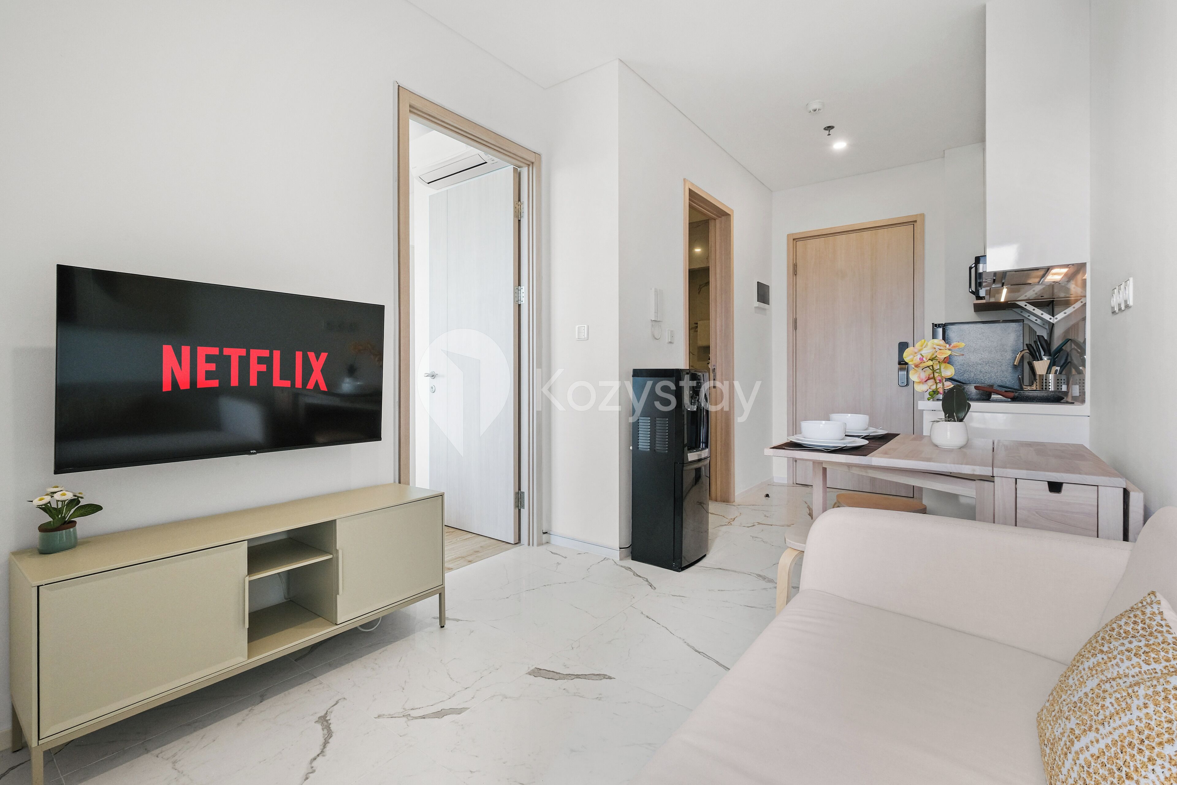 A modern living room with a flat-screen TV, a sofa, a coffee table, and a kitchen area in the background.