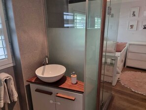 Ein modernes Badezimmer mit Duschkabine aus Glas, einem weißen Waschbecken und einer Holzauslage.