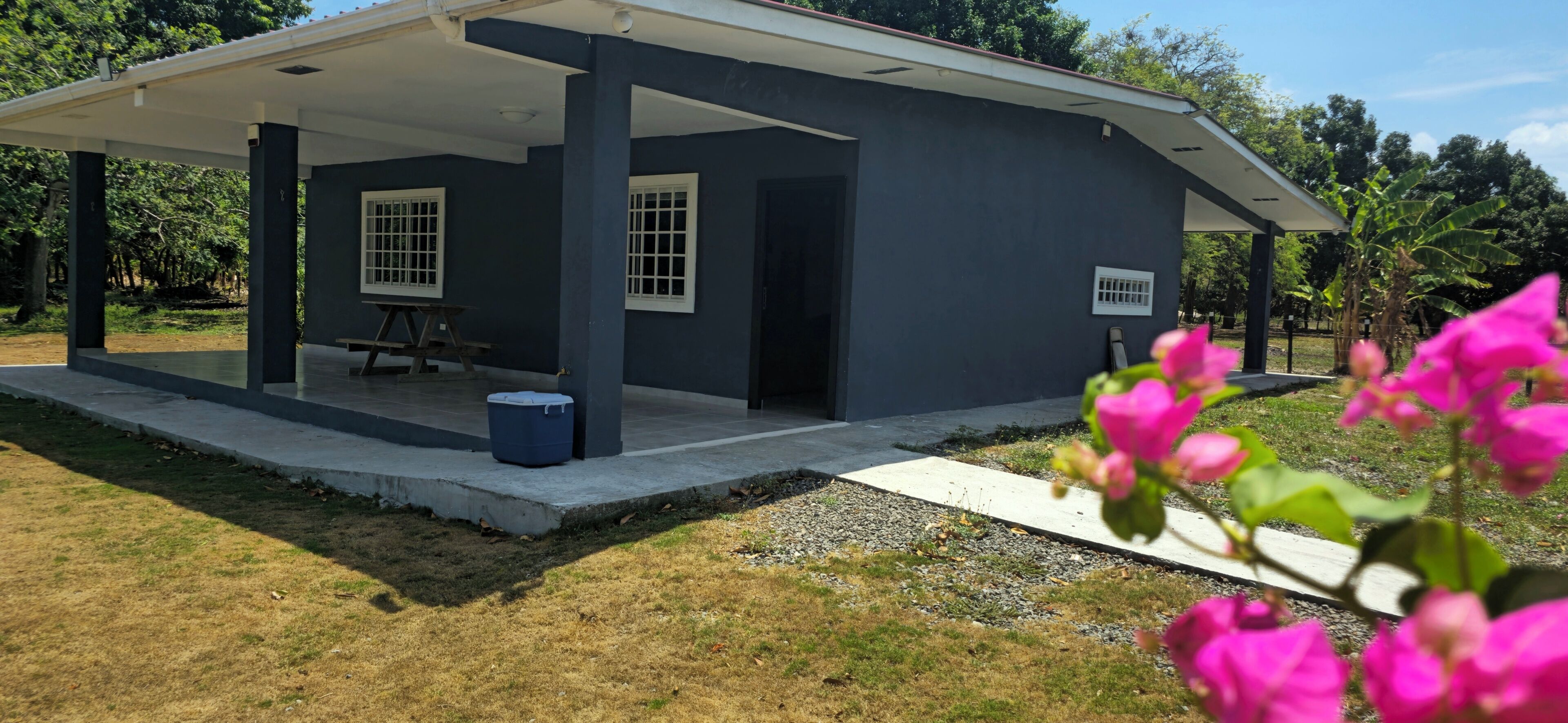 A building with a covered porch, two windows with bars, a bench, and a trash bin.
