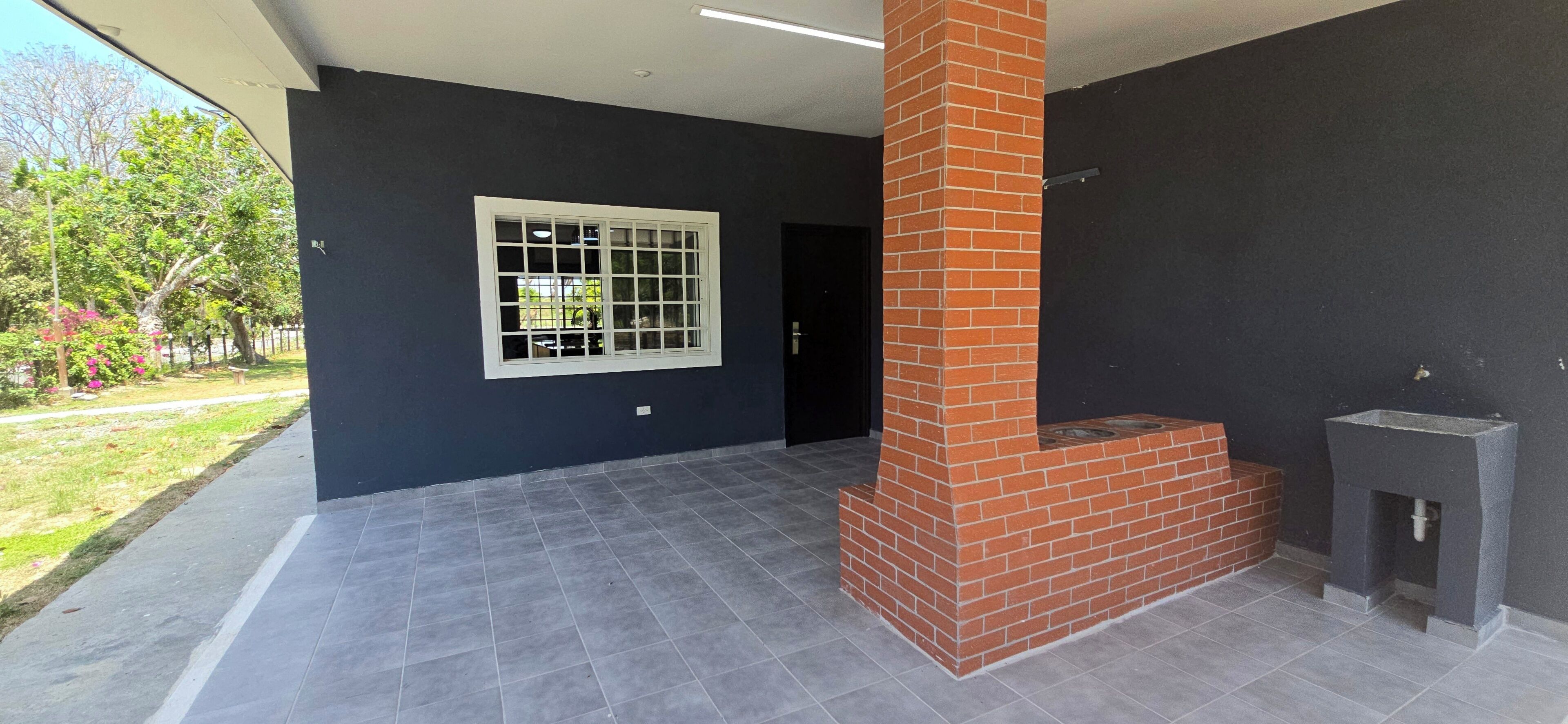 A room with a tiled floor, a window with a white frame, a brick chimney, and a small fireplace.