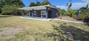 A single-story house with a covered porch, a small lawn, and surrounding vegetation. - Your Dream Escape to Nature & Fun at Villa Palmeras in Playa Juan Hombron (El Chiru)