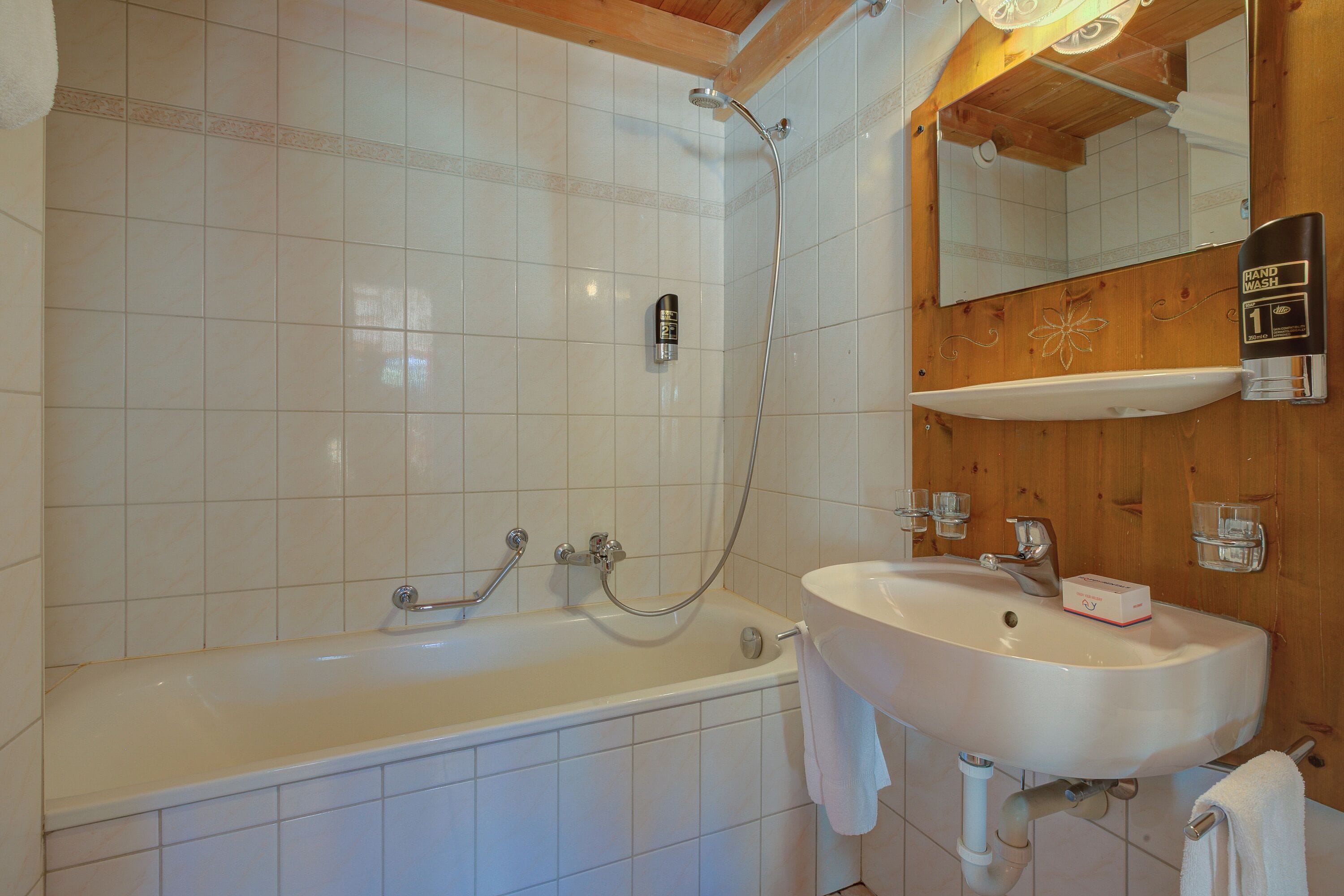 A bathroom with a bathtub, a sink, a hand wash station, and a mirror.