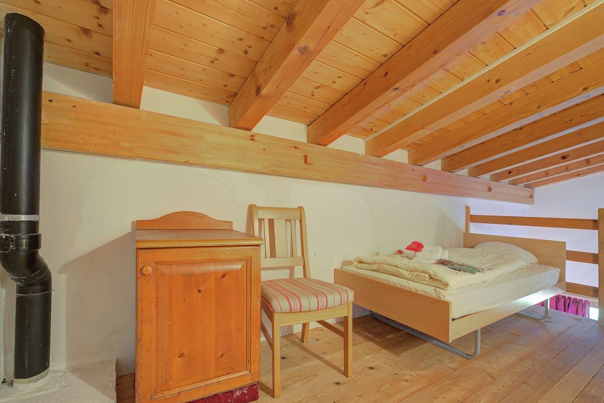 Un dormitorio con techo de madera, una cama, una silla, un armario de madera y un radiador.