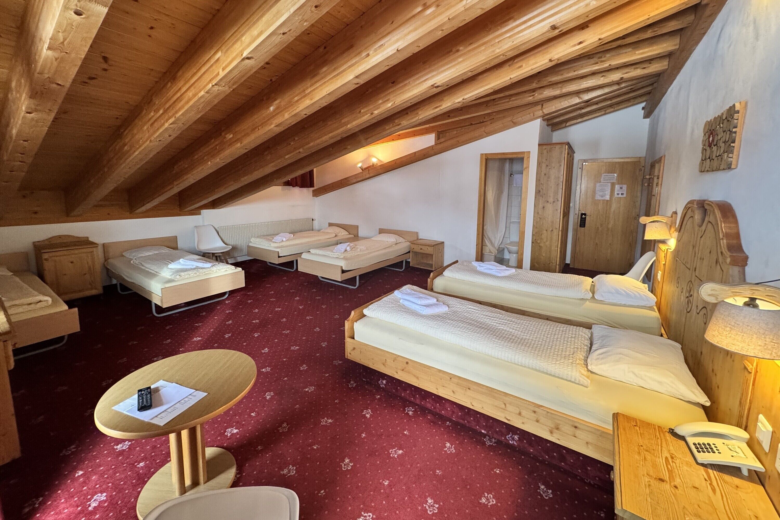 A cozy attic bedroom with wooden beams, two single beds, a small table, and a telephone.