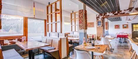 A restaurant with multiple dining areas, including a booth section and a table section. There are wooden chairs and tables, and the ceiling features a grid-like pattern.