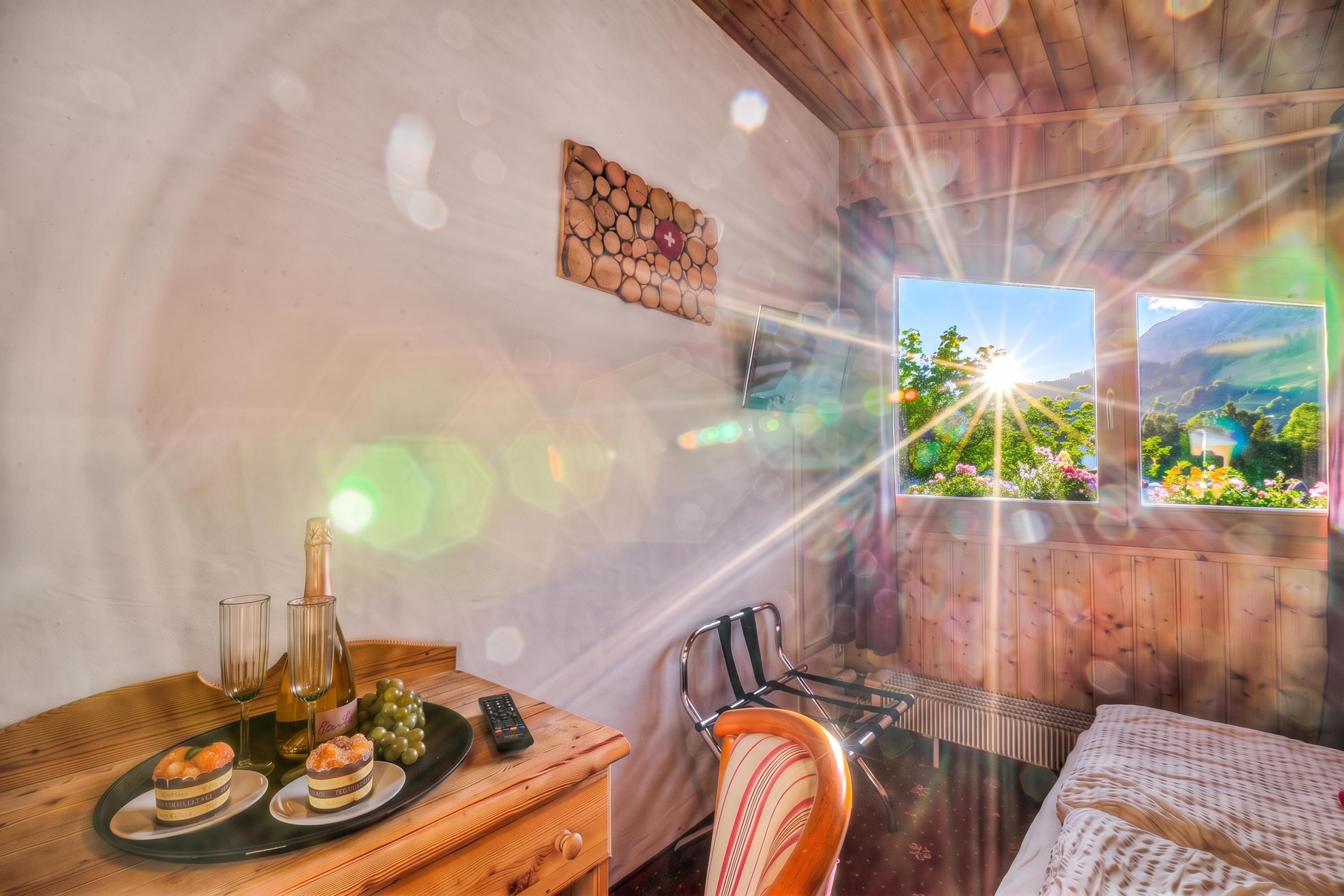 Un intérieur en bois avec une table à manger dressée, agrémentée de verres à vin, d’une bouteille et d’une assiette de nourriture. On y trouve une chaise et un lit recouvert d’une couvre-lit à motifs.