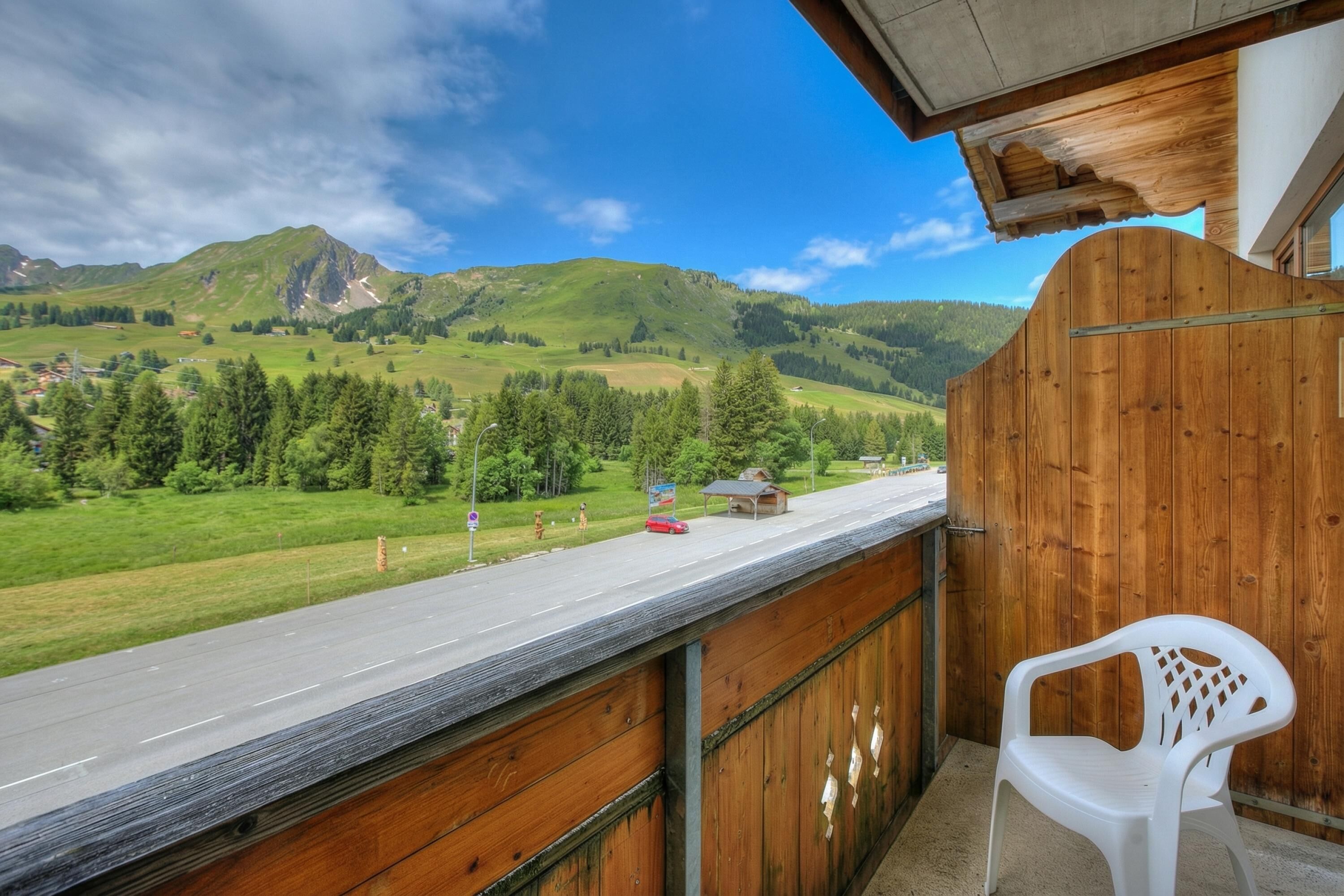 A balcony with a view of a road, green hills, and a small building.