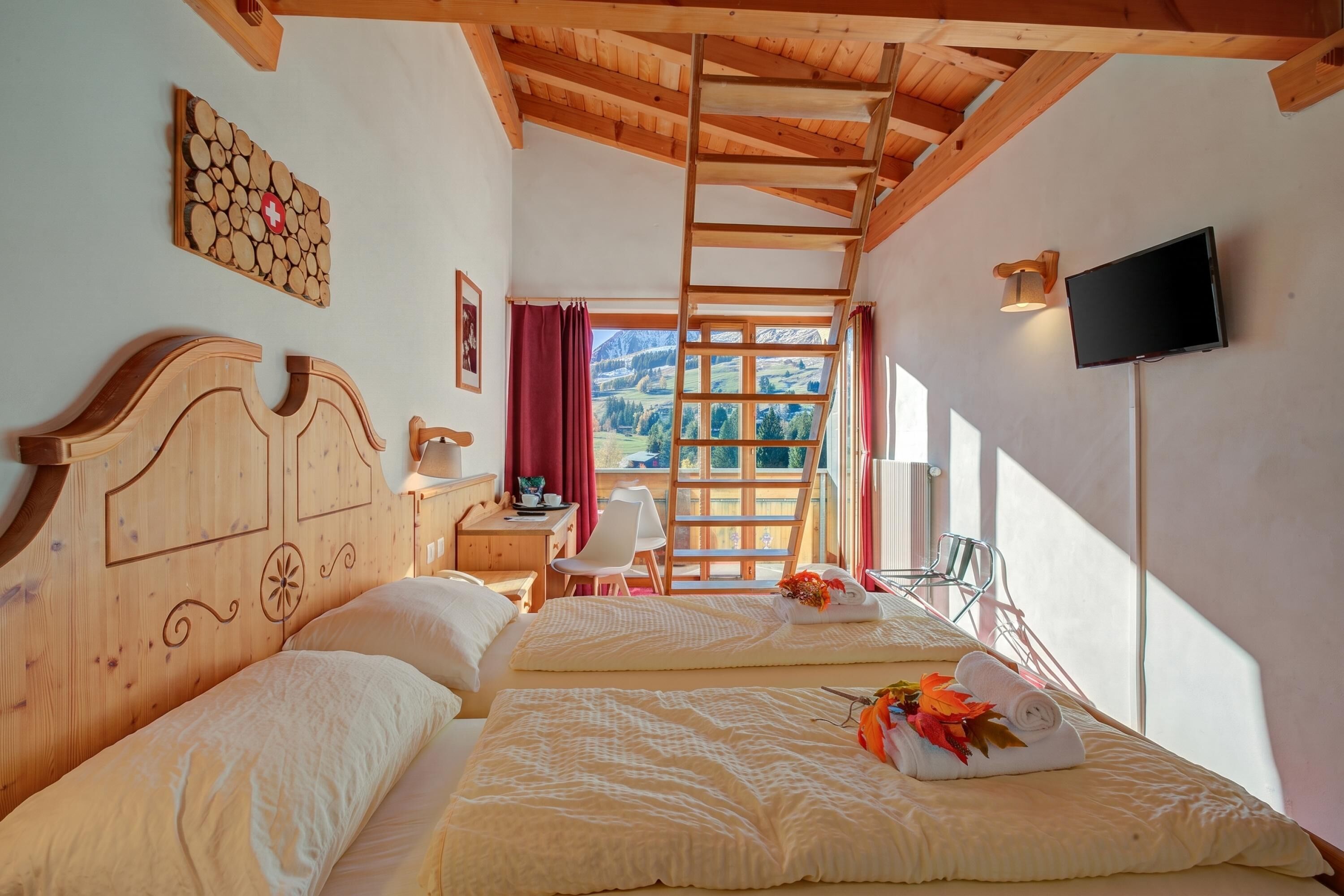 Ein Zimmer mit zwei Betten, einer Holzbalkendecke, einem Fernseher, einem Fenster mit Aussicht und einer Wanddekoration aus Holz.