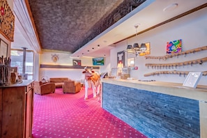 A hotel lobby with a red carpet, wooden furniture, a reception desk, and wall-mounted decor. - Hotel Relais Alpin (Ormont-Dessous)