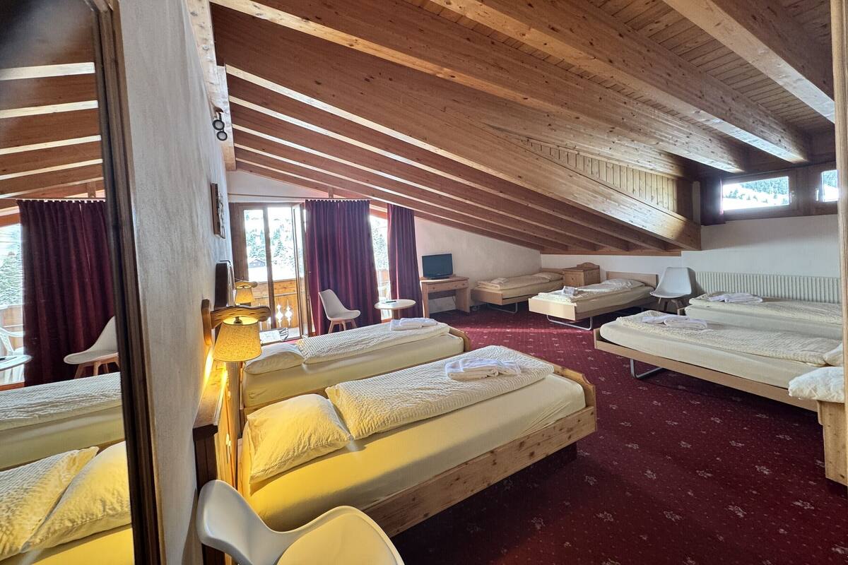 Una habitación con vigas de madera, dos camas, un escritorio, sillas y una ventana con cortinas.