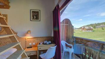 Ein Zimmer mit einem Holztisch, Stühlen, einem Bett, einem Fenster mit Blick auf Häuser und einem gerahmten Bild an der Wand.