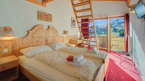 Habitación de hotel con dos camas, techo de madera, televisor, balcón con vistas y decoración de pared de madera.