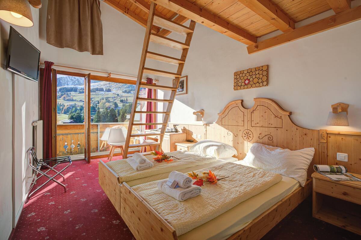 Una habitación de madera con una cama, una silla, una escalera y un televisor.