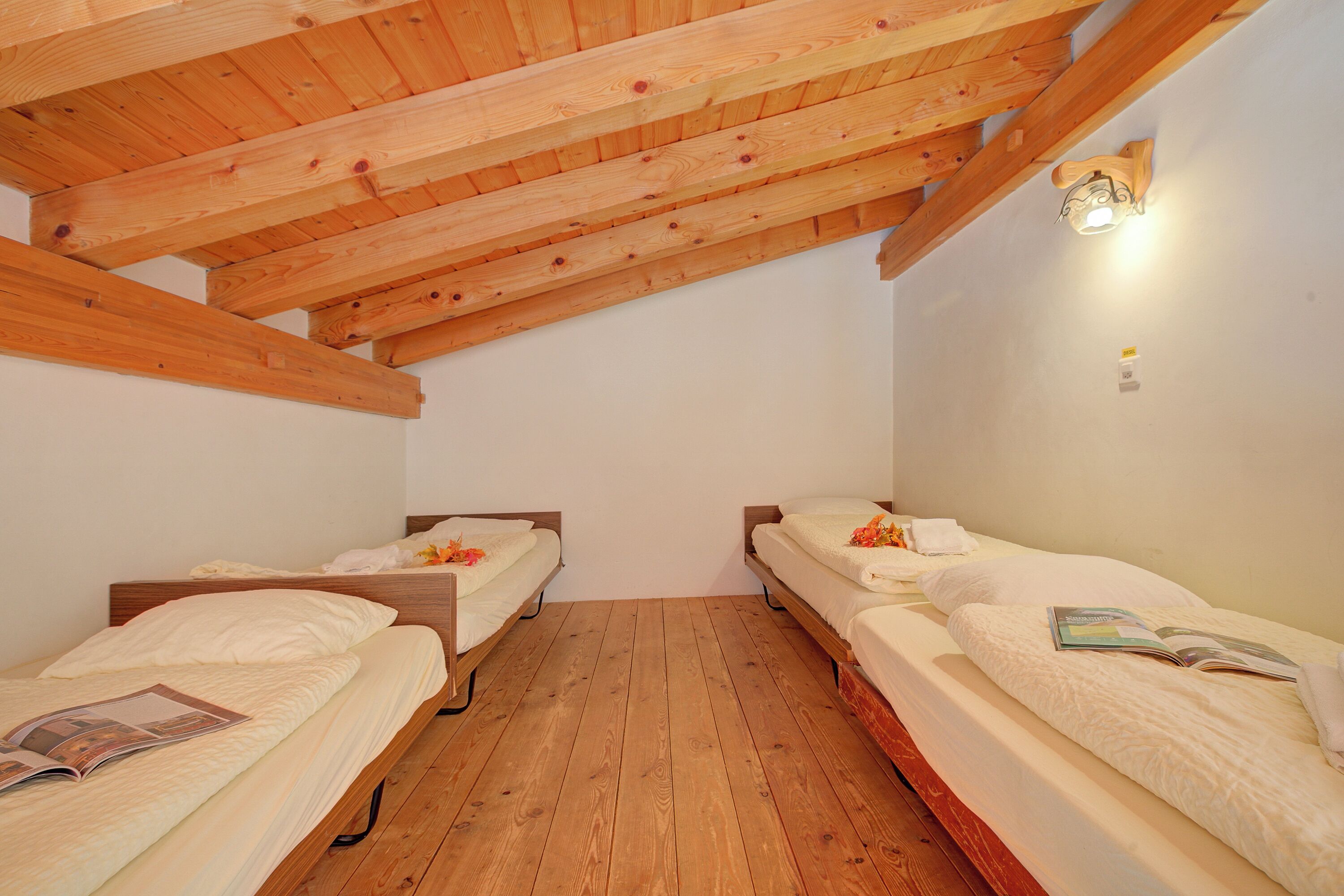 A small, wooden-floored room with two single beds, each with a pillow and a magazine on the bed.