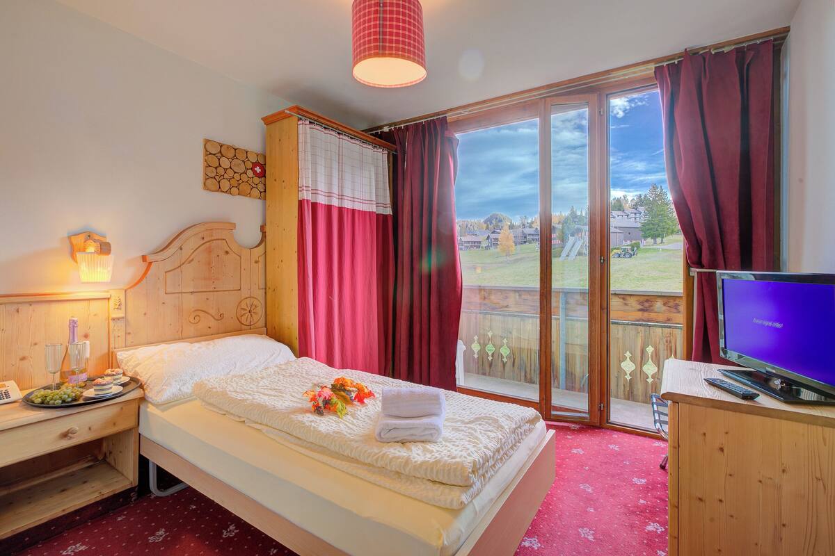 Habitación de hotel con una cama, televisión, escritorio con lámpara y vista al exterior.