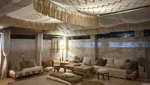 A cozy, rustic room with a brick wall, a large window, and a ceiling with a geometric pattern. There are several sofas and a small table, creating a comfortable seating area. - The Bagheera Retreat (Pushkar)