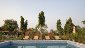 A swimming pool with tiled edges, surrounded by lounge chairs and tall trees. - The Bagheera Retreat (Pushkar)