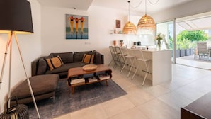Ein modernes Wohnzimmer mit einer Couch, einem Couchtisch und einem Essbereich mit Stühlen. An der Wand hängt ein Gemälde und ein großes Fenster sorgt für viel Licht.