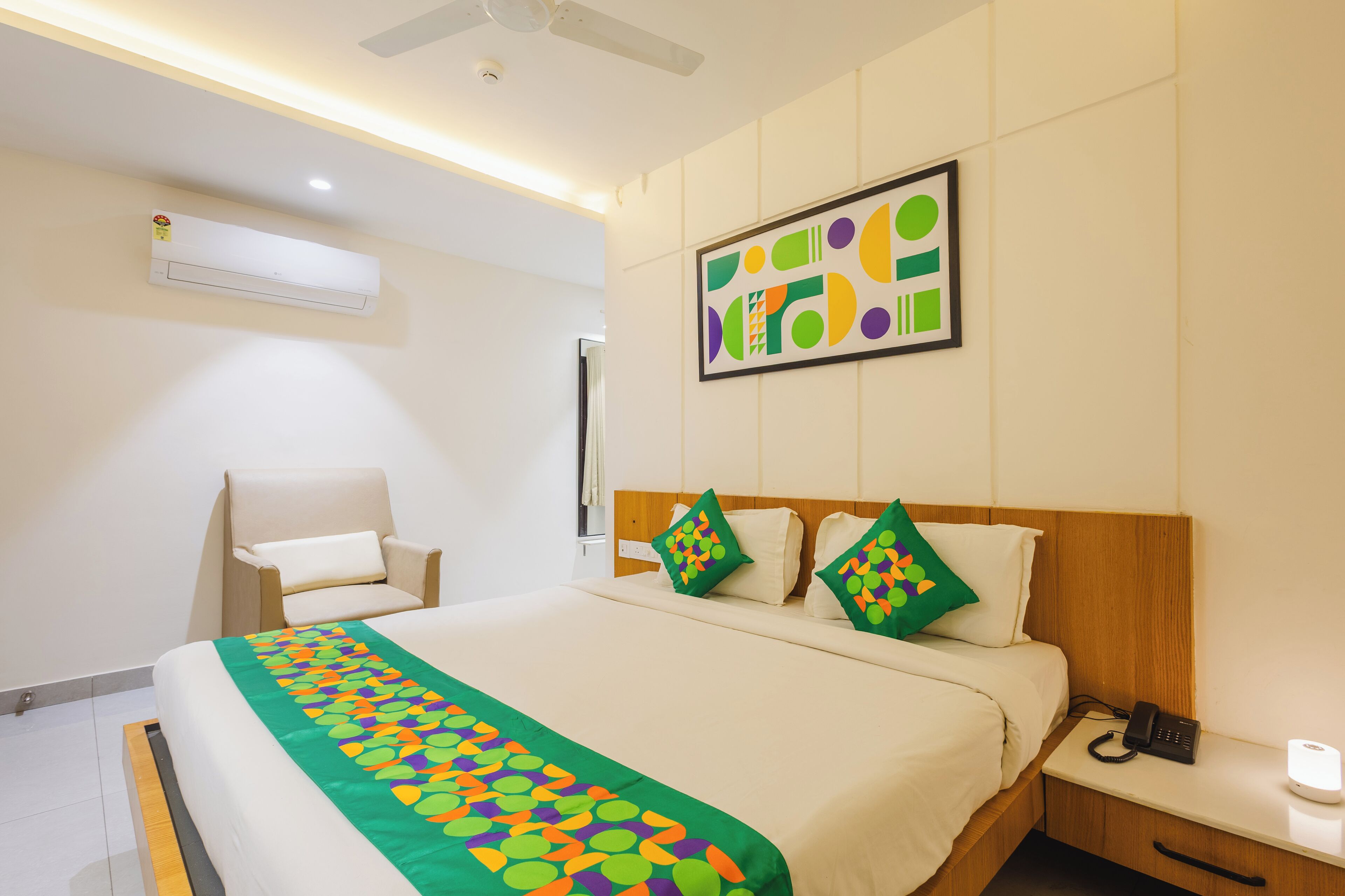 Habitación de hotel con cama, mesita de noche, silla y equipo de aire acondicionado.