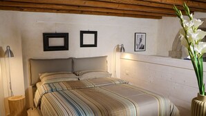 A bedroom with a bed, two framed pictures on the wall, a bedside lamp, and a vase with flowers.