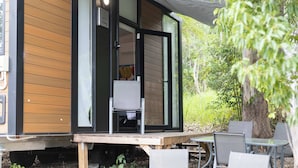 Une petite structure en bois dotée d’une porte coulissante en verre, d’une chaise et d’une table à l’extérieur.