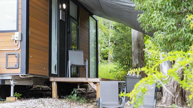 Un bâtiment moderne en bois, doté d’une grande porte coulissante, d’un espace extérieur aménagé et couvert, et offrant une vue sur la forêt environnante.