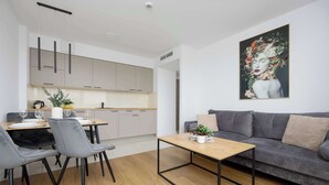 A modern living room with a grey sofa, a wooden coffee table, and a dining area with grey chairs and a table. - Functional Apartment | Large Balcony and Workspace (Warszawa)