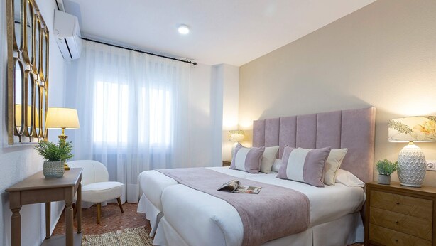 A hotel room with a large bed, a bedside table, a chair, a lamp, and a decorative mirror. - Spectacular Apartment in Cordoba Center. Avenida America (Córdoba)