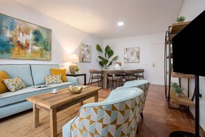 Uma sala de estar com sofá, mesa de centro, mesa de jantar e cadeiras, e uma escada.