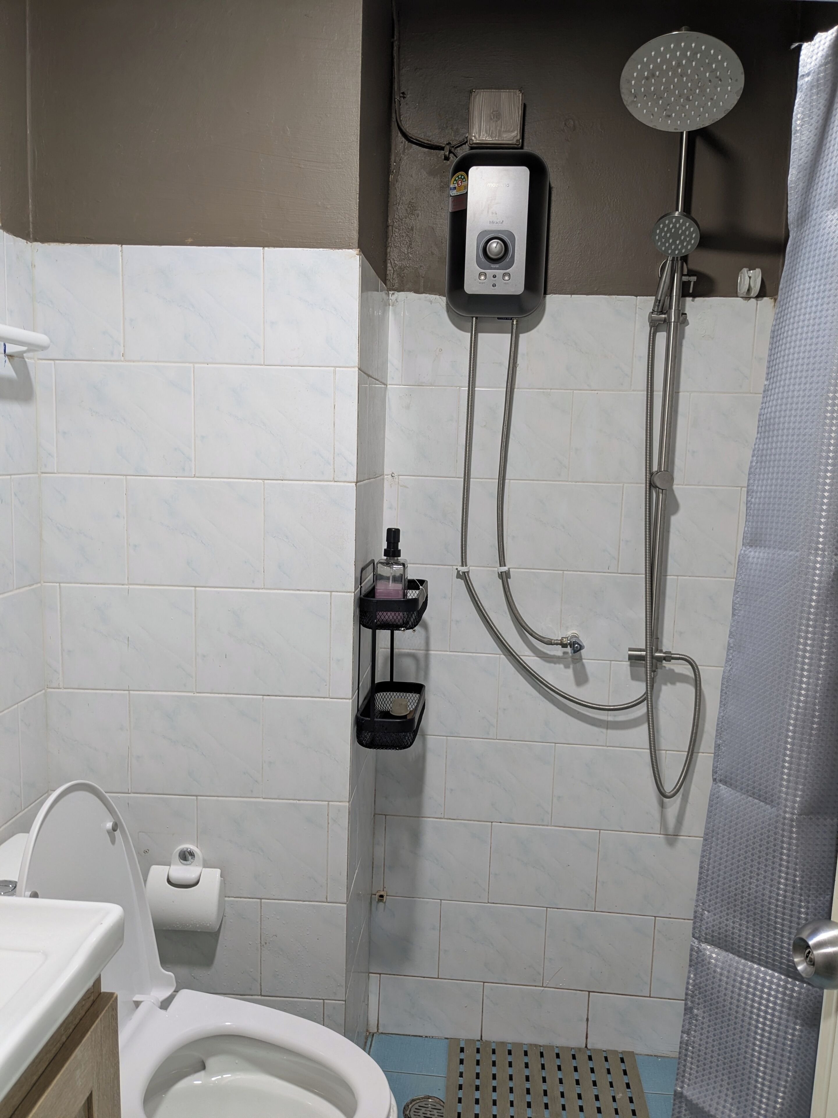 Et badeværelse med toilet, bruser med håndbruser og bøjle til håndklæder.