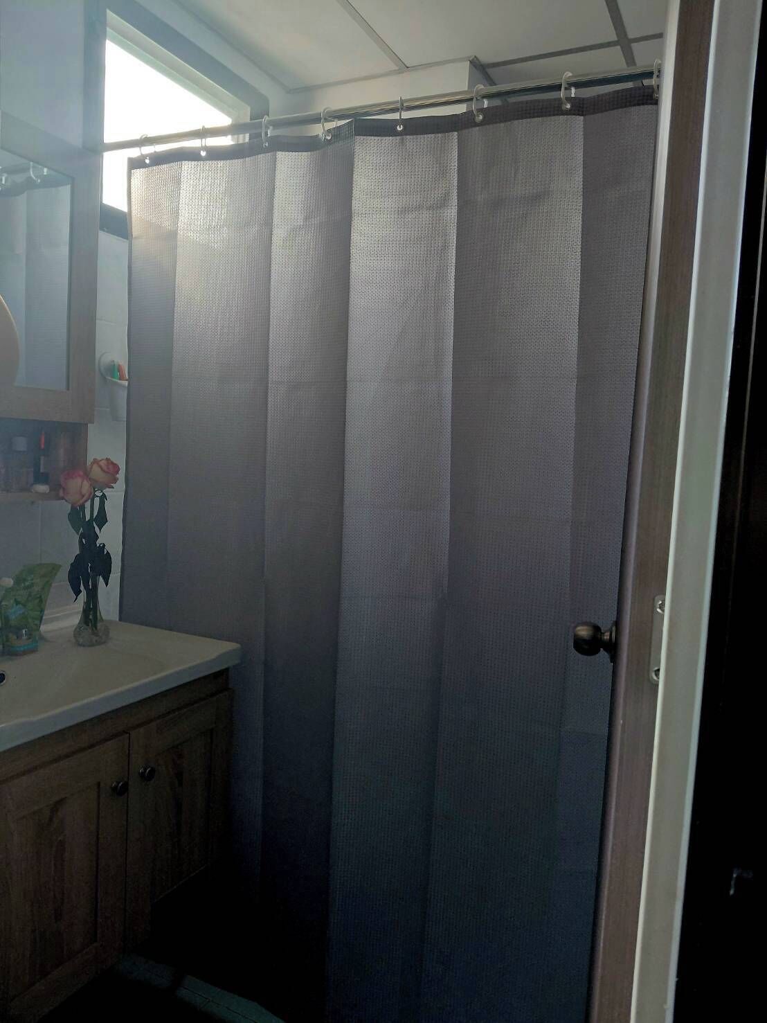 A bathroom with a shower curtain, a mirror, a sink with a vase of flowers, and wooden cabinets.
