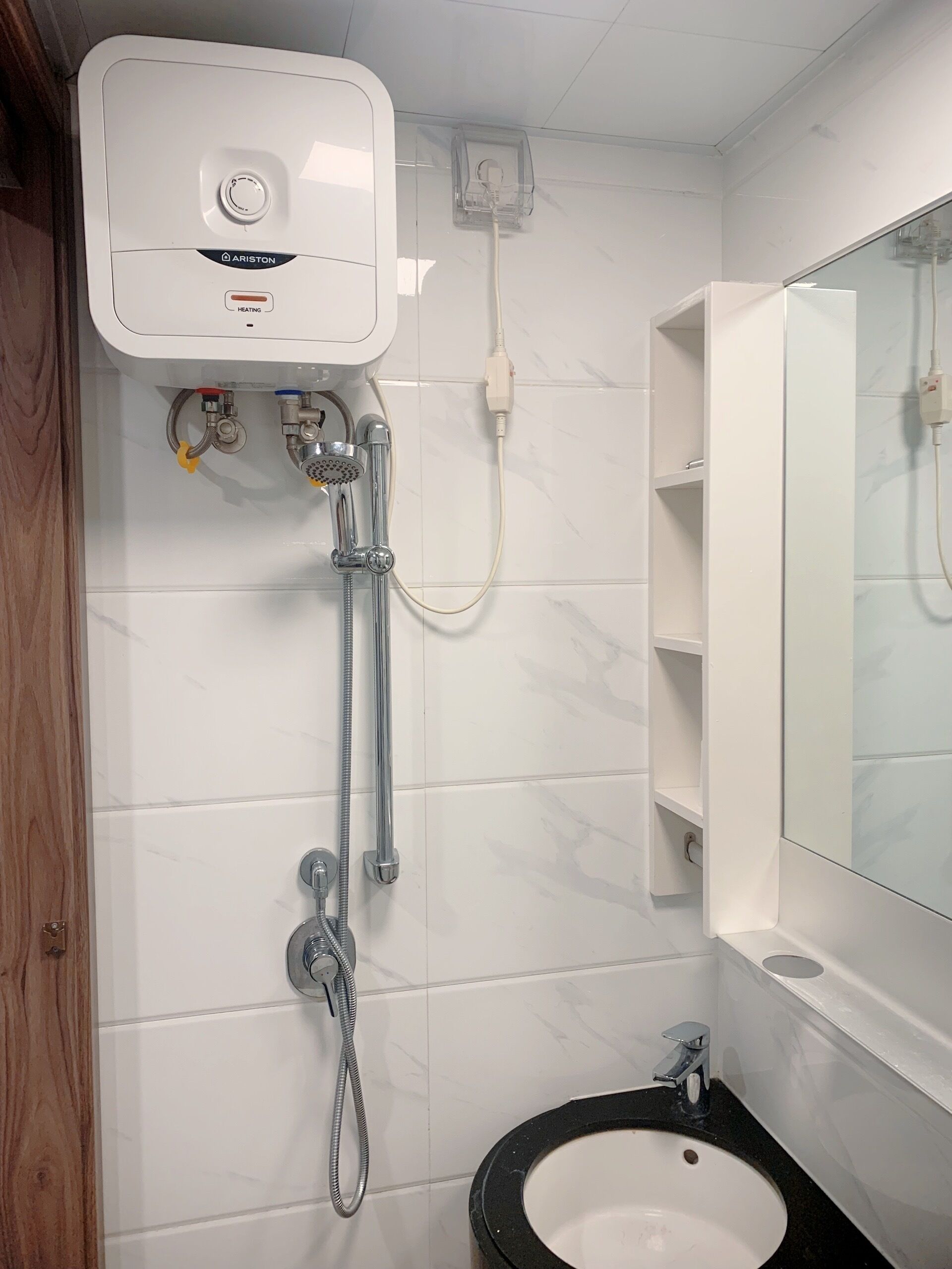 A bathroom with a white tiled wall, a white pedestal heater, a handheld showerhead, a sink with a black countertop, and a mirror above the sink.