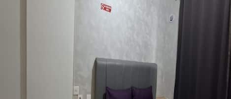Een slaapkamer met een bed, een nachtkastje, een stopcontact en een ‘Niet roken’-bord aan de muur.