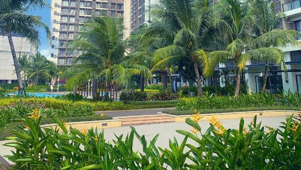 Un edificio residencial alto con múltiples balcones, rodeado de abundante vegetación y palmeras.