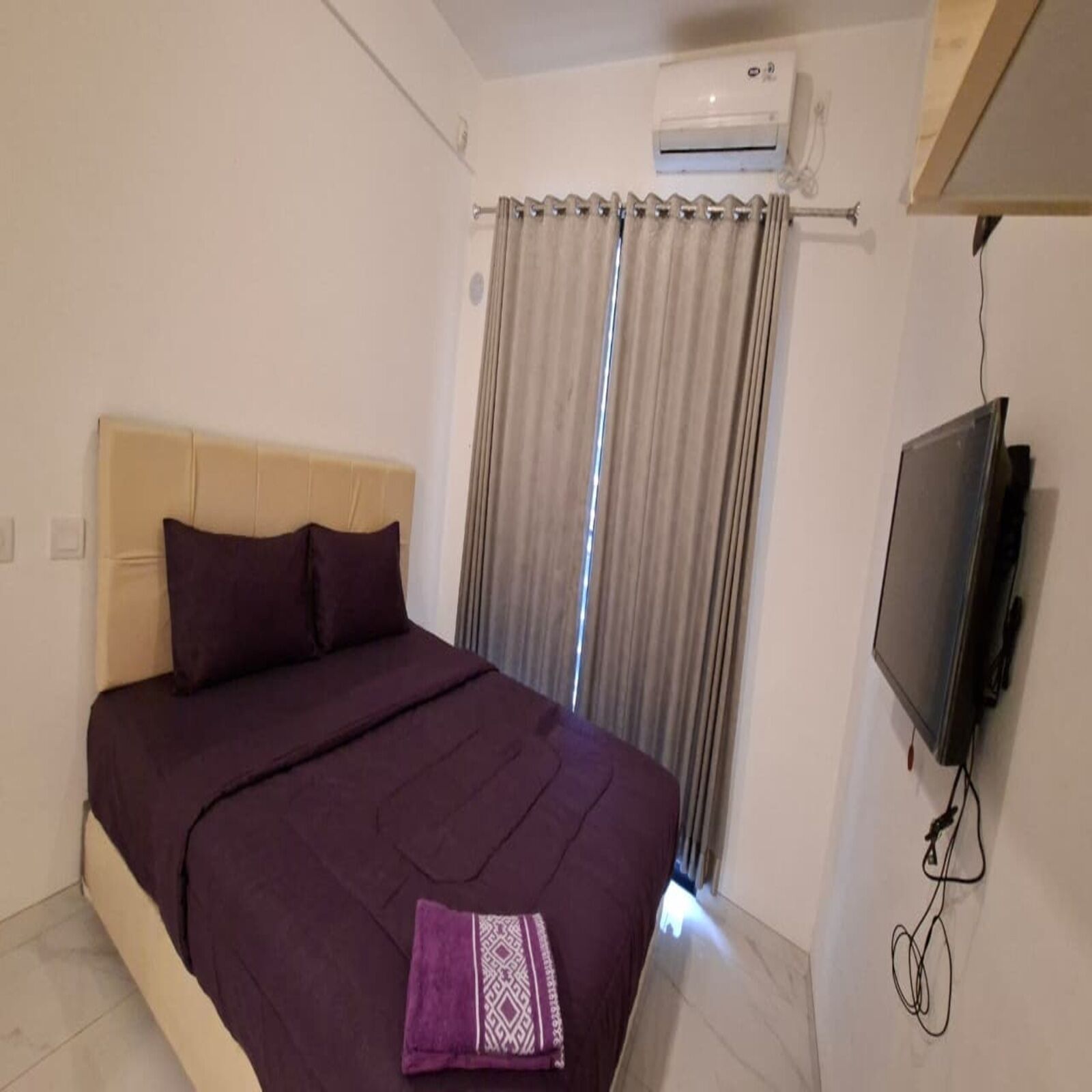A bedroom with a bed, a TV, an air conditioning unit, and a window with curtains.
