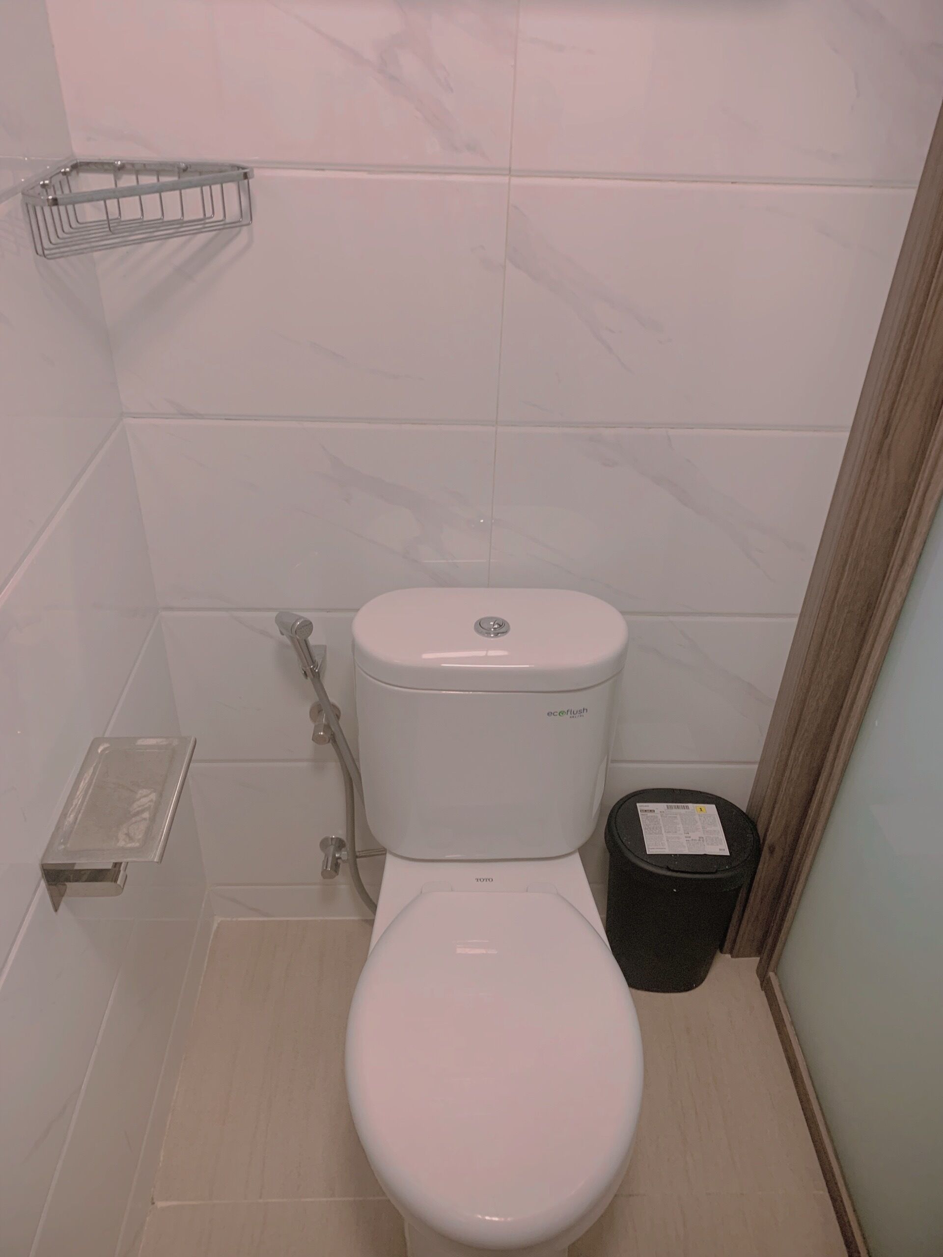 A small, clean bathroom with a white toilet, a shower area, and a trash bin.