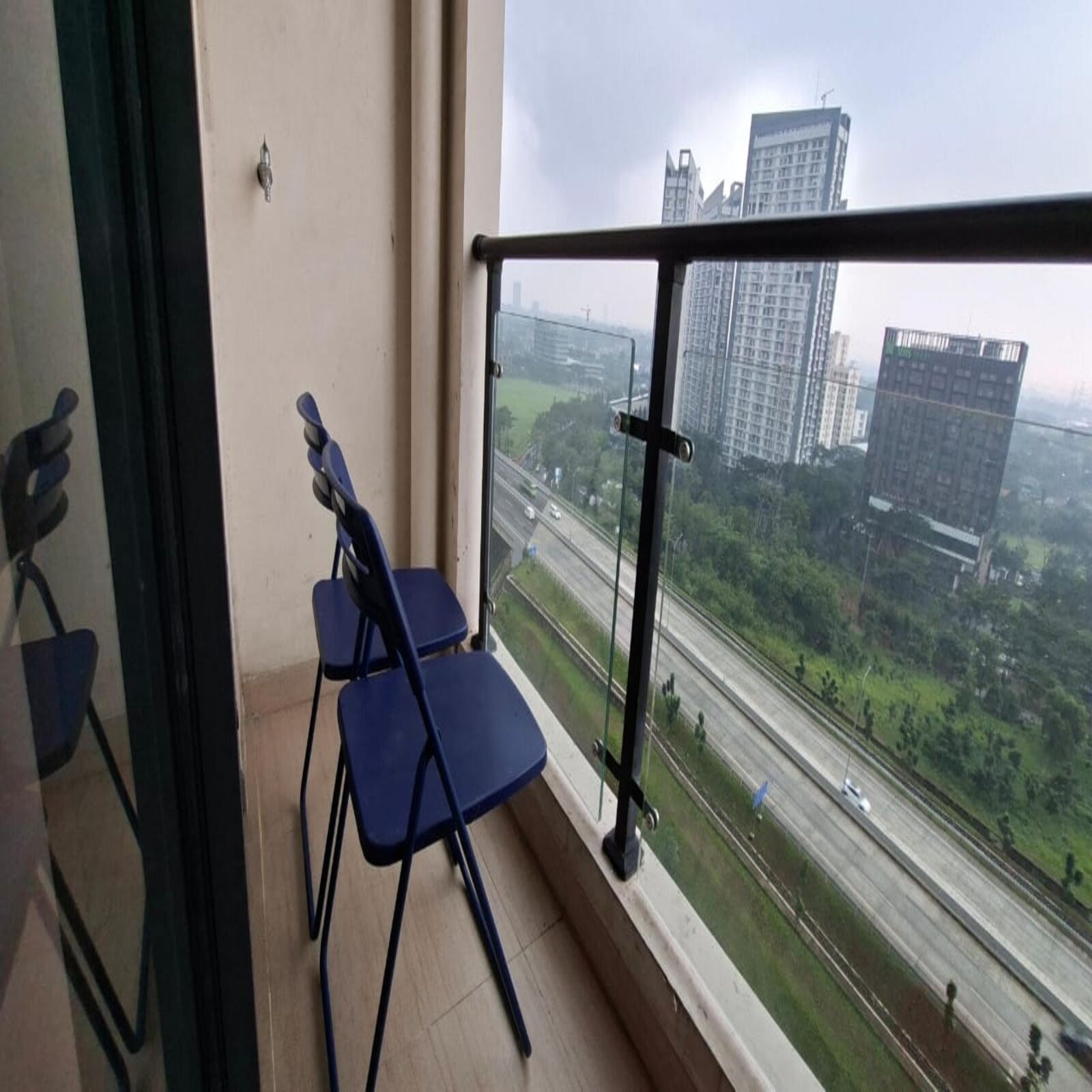 Un balcon avec deux chaises bleues et une vue sur une autoroute et des immeubles.