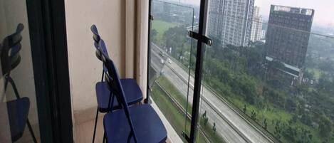 A balcony with two blue chairs and a view of a highway and buildings.