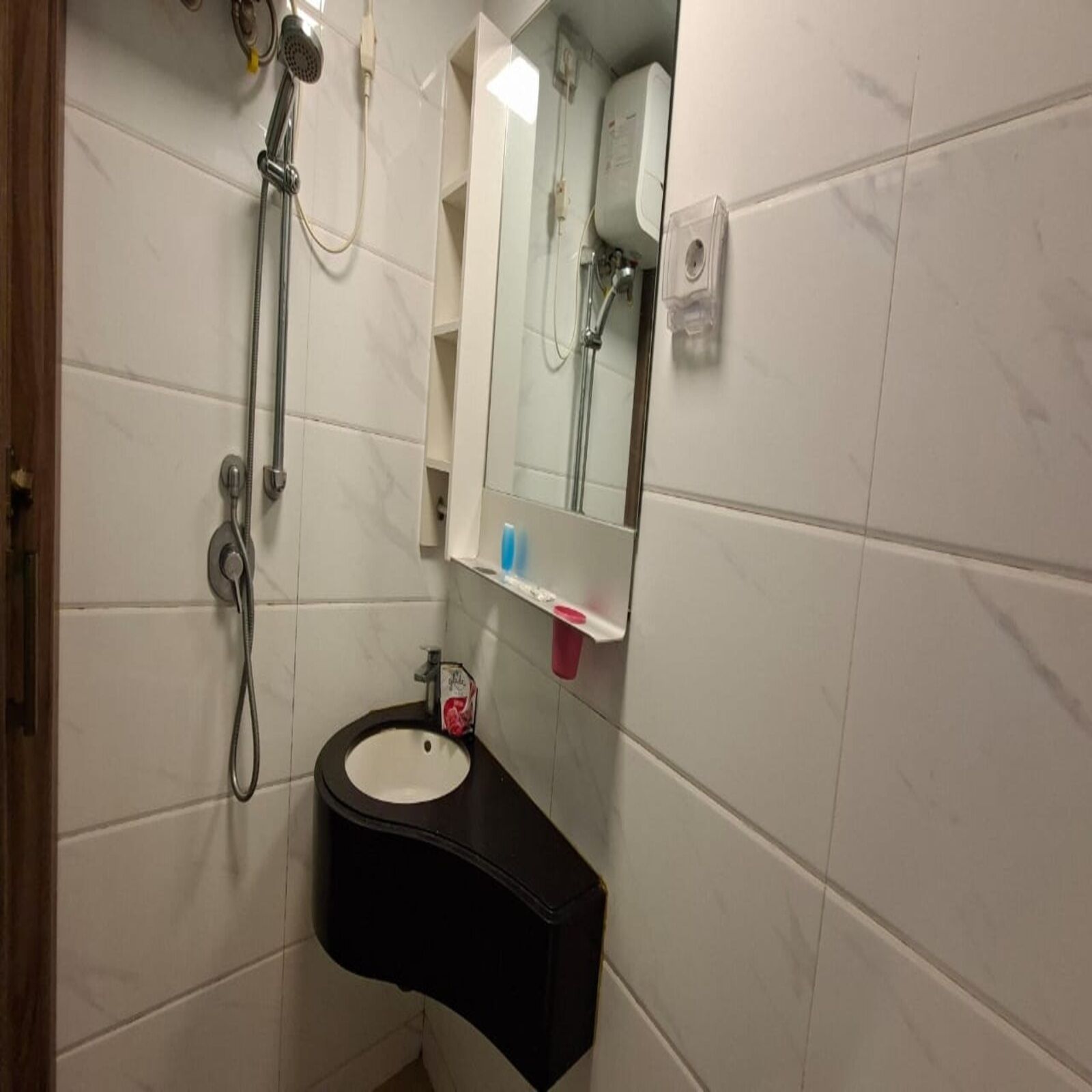 A bathroom with a white tiled wall, a black sink, a mirror, and a shower head.