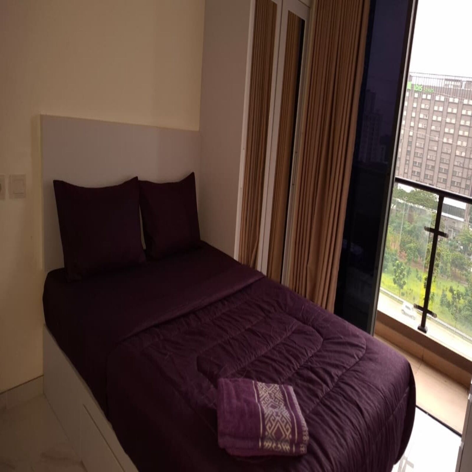 A bedroom with a large bed, a window with curtains, and a view of a building outside.