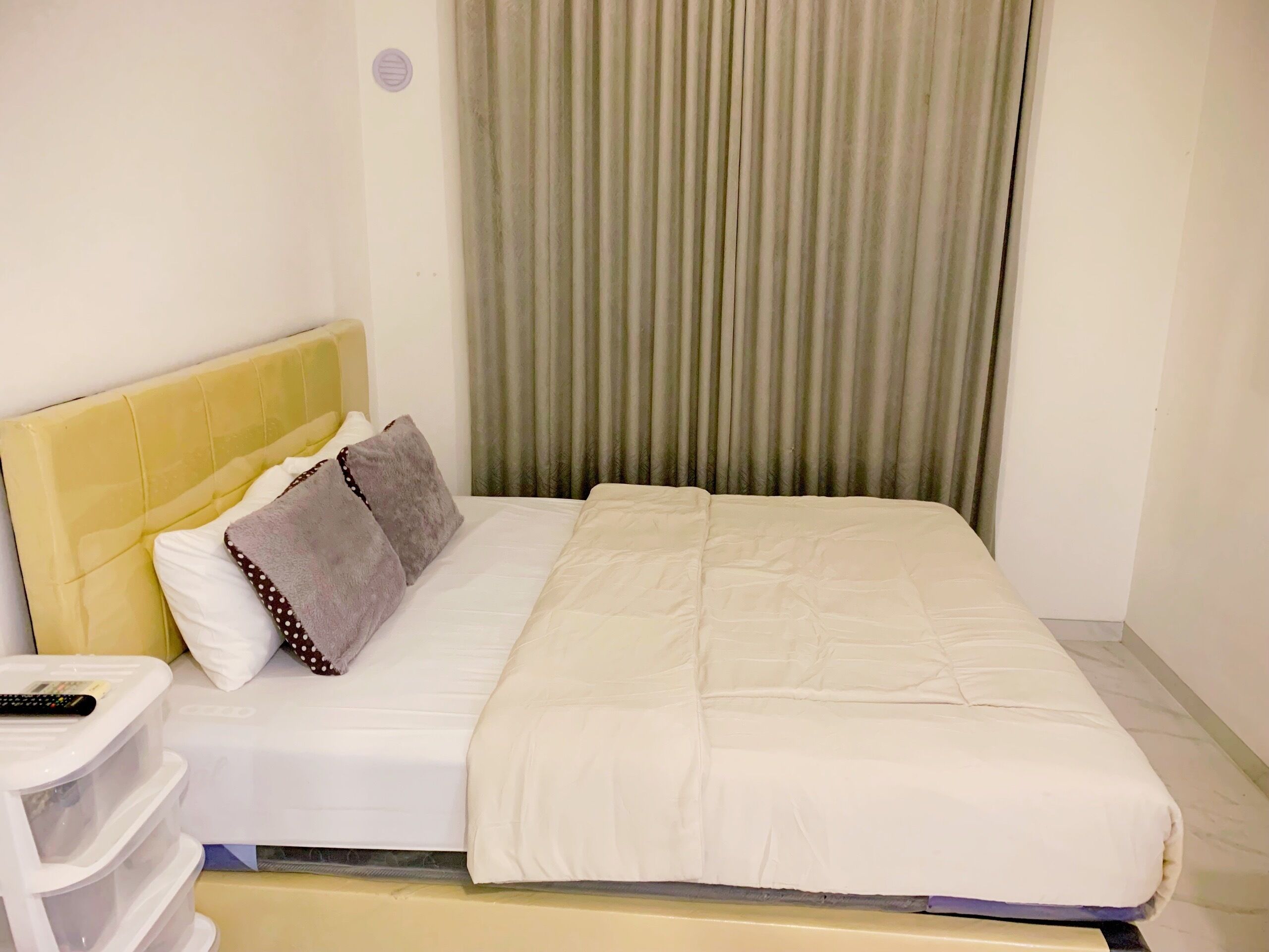 A hotel room with a bed, a nightstand, a remote control, and a window with curtains.