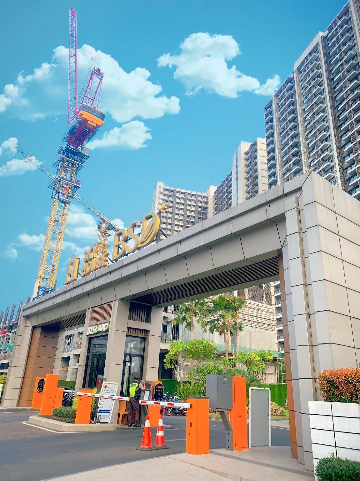 A modern building with a prominent sign, a pedestrian overpass, and a construction crane in the background.